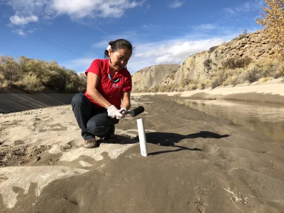 Woman in a river bed collecting a soil sample