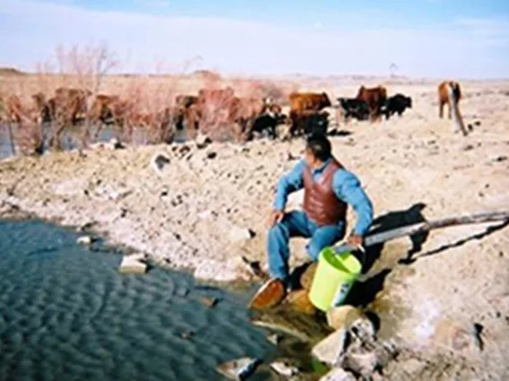 Man crouched next to a stream with a bucket